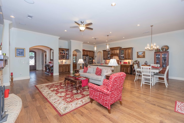 living room with ceiling fan with notable chandelier, ornamental molding, and light hardwood / wood-style flooring