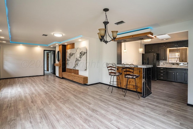 1802 Chama St, Amarillo, TX 79102 - kitchen with a breakfast bar area, black fridge, a chandelier, light wood finished floors, and recessed lighting