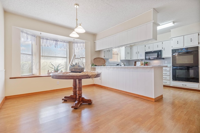 kitchen with light countertops, white cabinetry, a peninsula, black appliances, and light wood-style floors