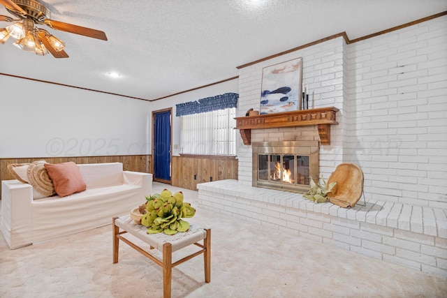 carpeted living area with a textured ceiling, wood walls, a brick fireplace, ornamental molding, and wainscoting
