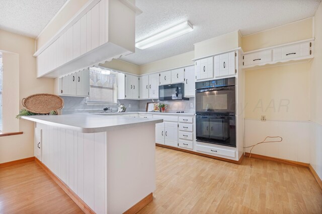 kitchen featuring a textured ceiling, light wood-style flooring, light countertops, a peninsula, and black appliances