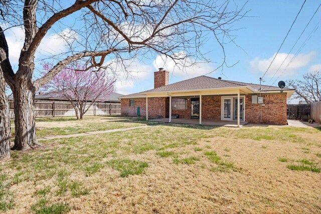 rear view of house with a chimney, french doors, a fenced backyard, brick siding, and a patio area