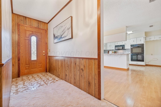 foyer entrance featuring light wood-type flooring, a textured ceiling, wood walls, and wainscoting