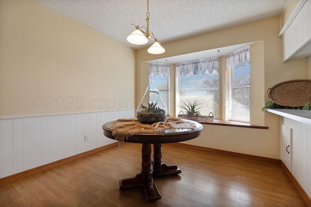 dining area with a wainscoted wall, a textured ceiling, and wood finished floors