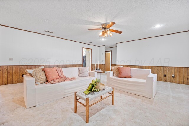 carpeted living room featuring wooden walls, a textured ceiling, wainscoting, visible vents, and ceiling fan