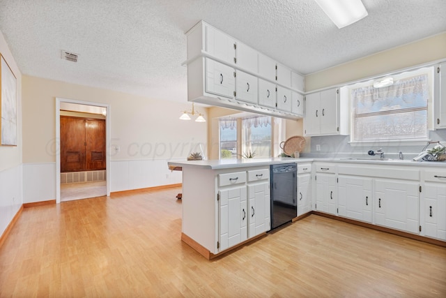 kitchen with a wainscoted wall, a sink, a peninsula, black dishwasher, and a healthy amount of sunlight