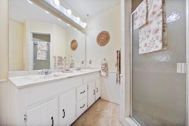 bathroom with a shower stall, double vanity, a sink, and a textured ceiling