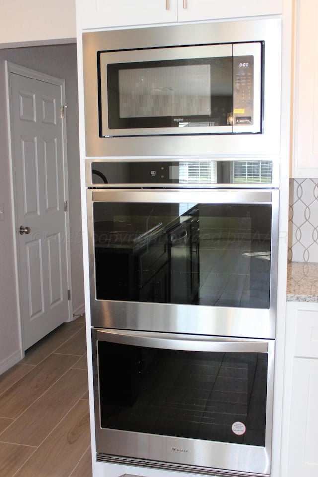 interior details with light stone countertops, stainless steel appliances, white cabinetry, and tasteful backsplash