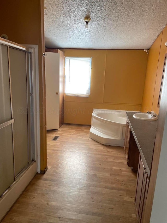 bathroom featuring a textured ceiling, wood finished floors, a garden tub, and a stall shower