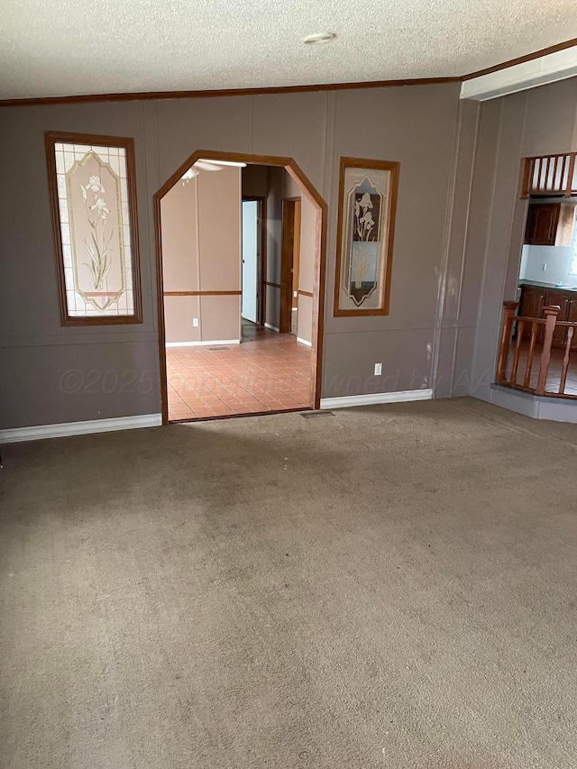 unfurnished room with a decorative wall, ornamental molding, a textured ceiling, and carpet