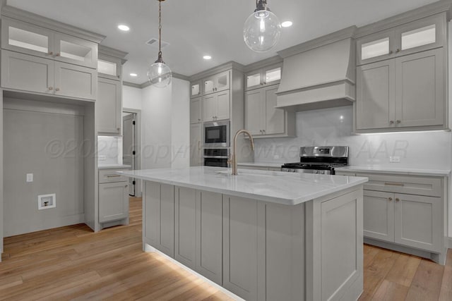 5505 Sheridan St, Amarillo, TX 79119 - kitchen featuring stainless steel appliances, custom range hood, light wood finished floors, an island with sink, and light stone countertops