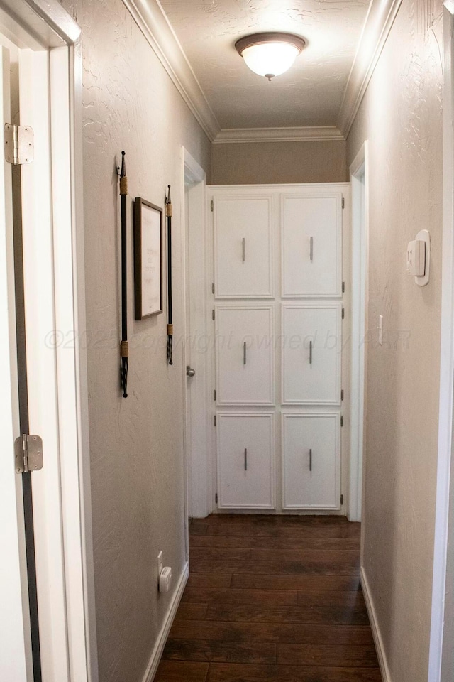 hallway featuring a textured wall, dark wood-style flooring, baseboards, and ornamental molding