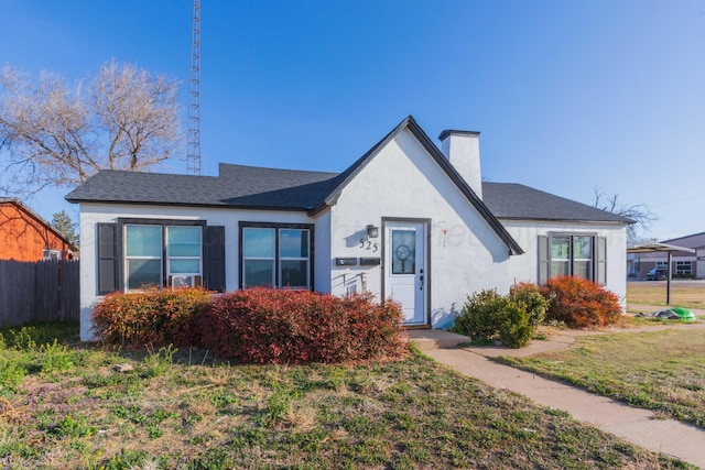 view of front of home featuring fence, a chimney, roof with shingles, and stucco siding