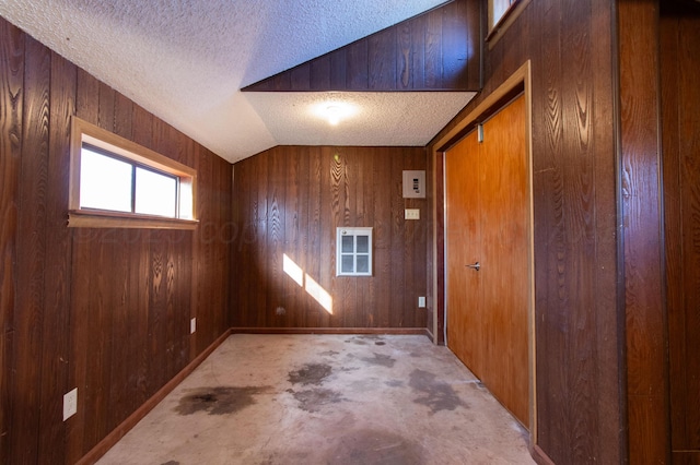 interior space with wood walls, vaulted ceiling, and a textured ceiling