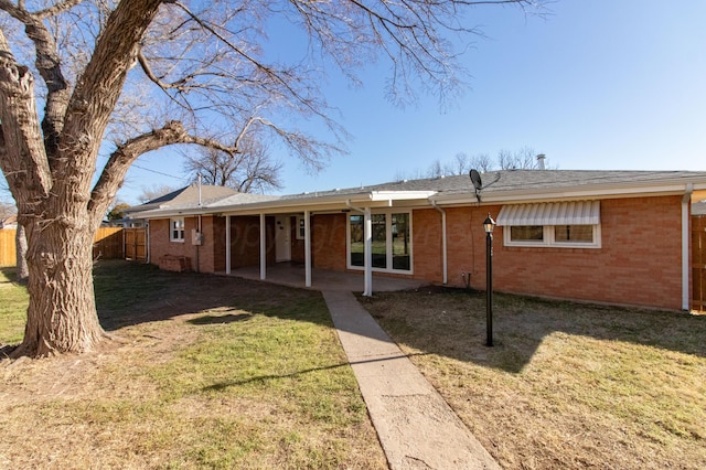 rear view of property featuring a patio area, brick siding, a yard, and fence