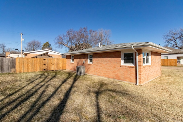 view of home's exterior with central air condition unit, brick siding, fence, and a lawn