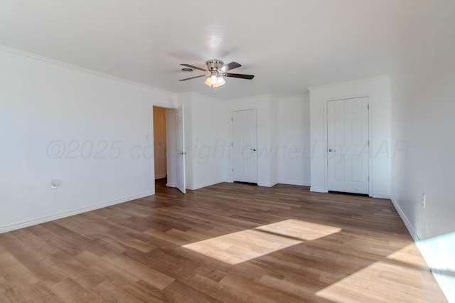 unfurnished bedroom with ceiling fan, crown molding, baseboards, and wood finished floors