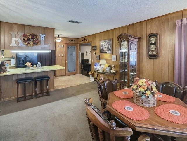 dining room featuring ceiling fan, wooden walls, a textured ceiling, and dark carpet