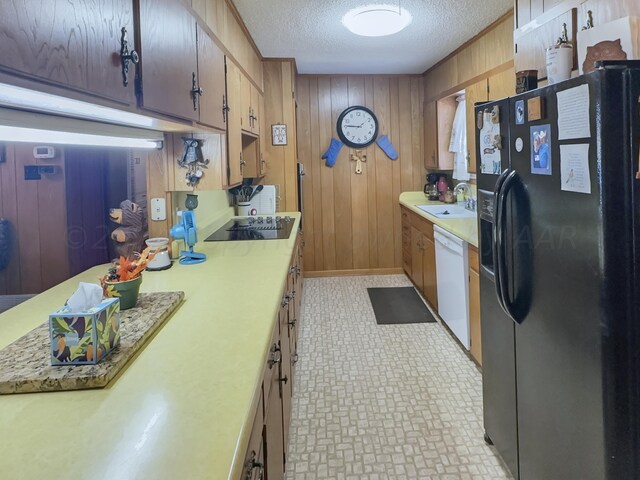 kitchen featuring black appliances, wood walls, sink, and a textured ceiling