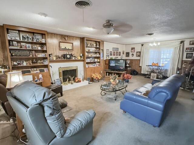 living room featuring wooden walls, a textured ceiling, carpet floors, and ceiling fan with notable chandelier