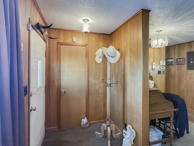 entryway featuring wood walls, a textured ceiling, a notable chandelier, and carpet