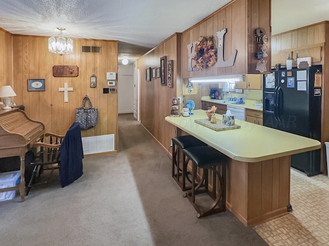 kitchen featuring light carpet, a kitchen bar, hanging light fixtures, wooden walls, and black fridge with ice dispenser