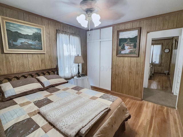 bedroom with light hardwood / wood-style floors, ceiling fan, wooden walls, and a closet