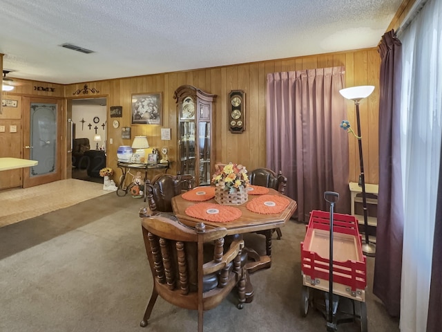 dining room featuring wooden walls, a textured ceiling, and carpet floors