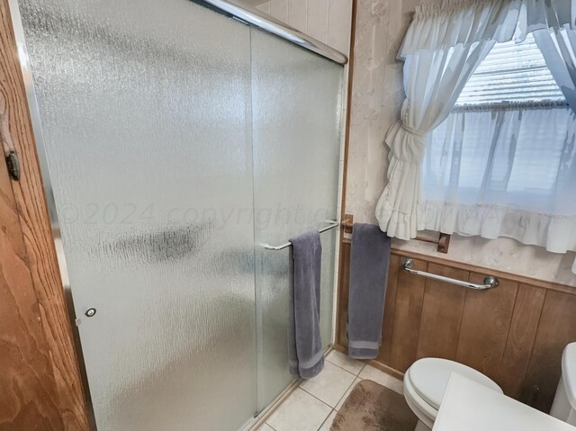 bathroom featuring toilet, an enclosed shower, wood walls, and tile patterned floors