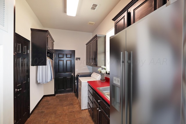 kitchen with high end refrigerator, washer and clothes dryer, dark brown cabinetry, baseboards, and visible vents
