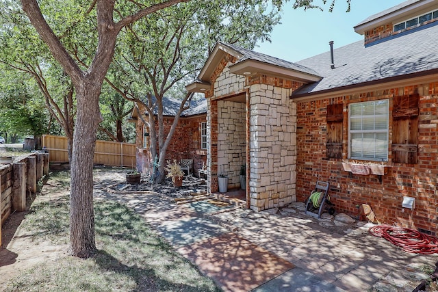 exterior space with fence, a patio area, roof with shingles, and brick siding