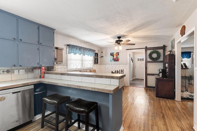 kitchen with a ceiling fan, a peninsula, a barn door, blue cabinets, and dishwasher