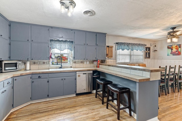 kitchen with light wood-style floors, a sink, a peninsula, and stainless steel appliances
