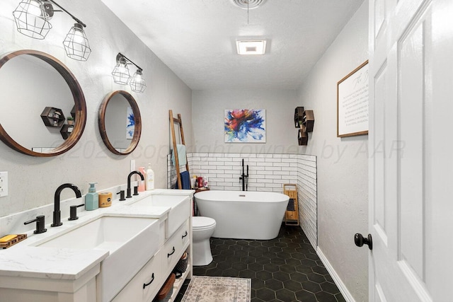 full bathroom featuring double vanity, a textured ceiling, a freestanding bath, a sink, and a textured wall