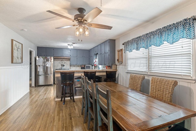dining area with a ceiling fan, wainscoting, light wood-type flooring, and a textured ceiling
