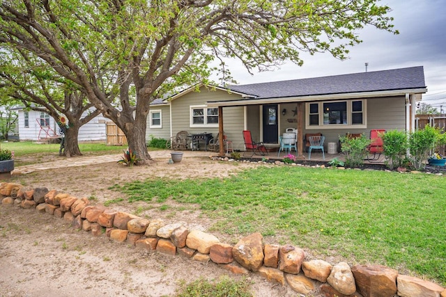 view of front of house featuring roof with shingles, fence, covered porch, and a front yard