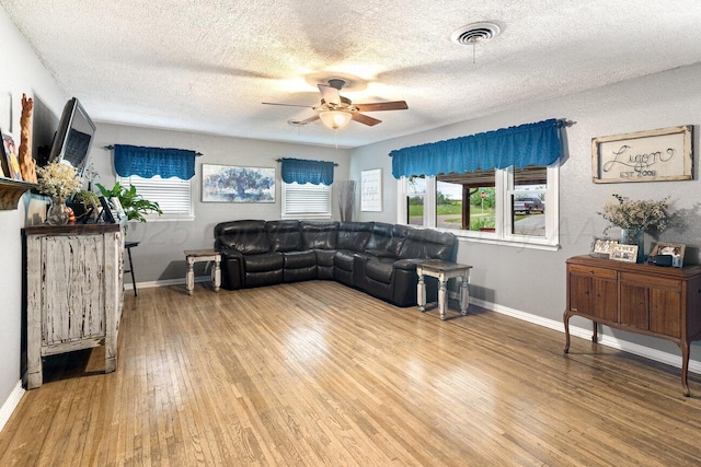 living area with light wood-style floors, a textured ceiling, a ceiling fan, baseboards, and visible vents