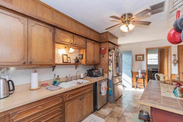 kitchen featuring sink, appliances with stainless steel finishes, ceiling fan, a textured ceiling, and decorative backsplash