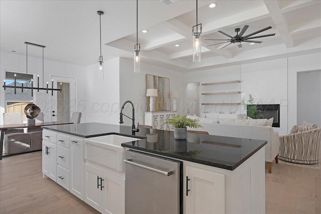 kitchen with a center island with sink, light wood finished floors, stainless steel dishwasher, a sink, and coffered ceiling