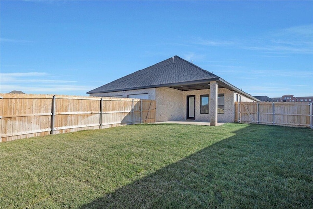 back of house with a shingled roof, a fenced backyard, a yard, and a patio