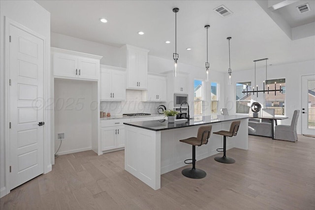 kitchen with light wood finished floors, a center island with sink, visible vents, and white cabinetry