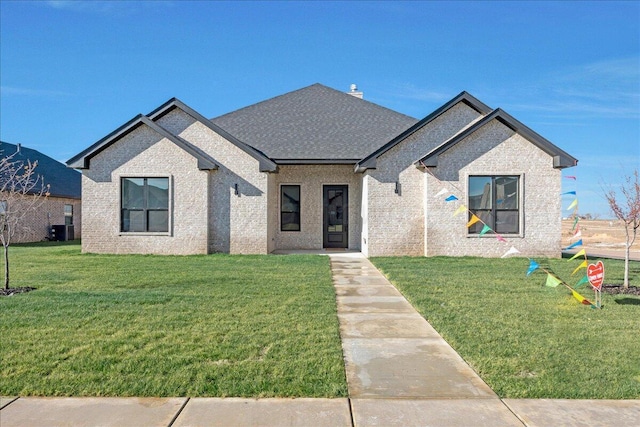 view of front of house featuring a shingled roof, brick siding, a front lawn, and central air condition unit