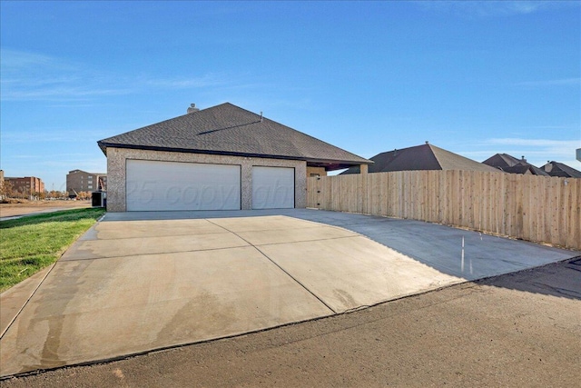 exterior space with an attached garage, a shingled roof, fence, and concrete driveway