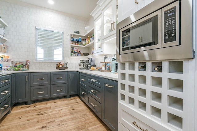 kitchen featuring white cabinets, light wood-type flooring, tasteful backsplash, and stainless steel microwave