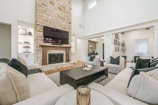 living room with a stone fireplace, hardwood / wood-style floors, a towering ceiling, and built in features