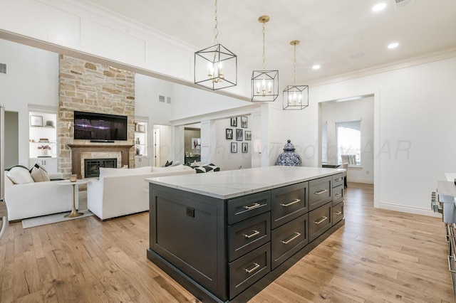 kitchen featuring a center island, hanging light fixtures, a stone fireplace, light stone counters, and light wood-type flooring