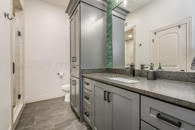 bathroom featuring a shower with door, vanity, and toilet