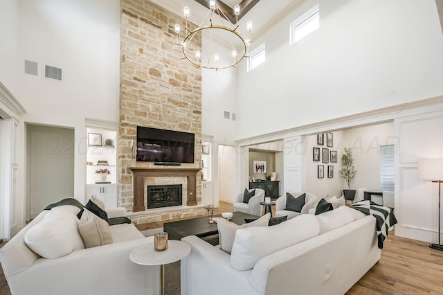 living room with a stone fireplace, a towering ceiling, a chandelier, and light wood-type flooring