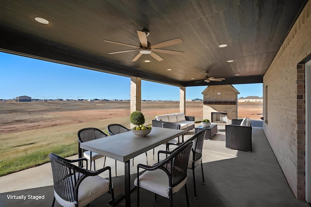 view of patio / terrace with an outdoor living space with a fireplace, ceiling fan, and a rural view