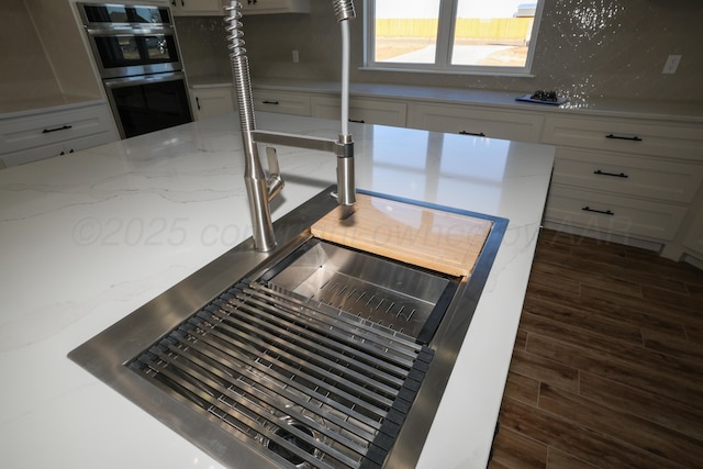 interior details with stainless steel double oven, dark hardwood / wood-style floors, and light stone counters